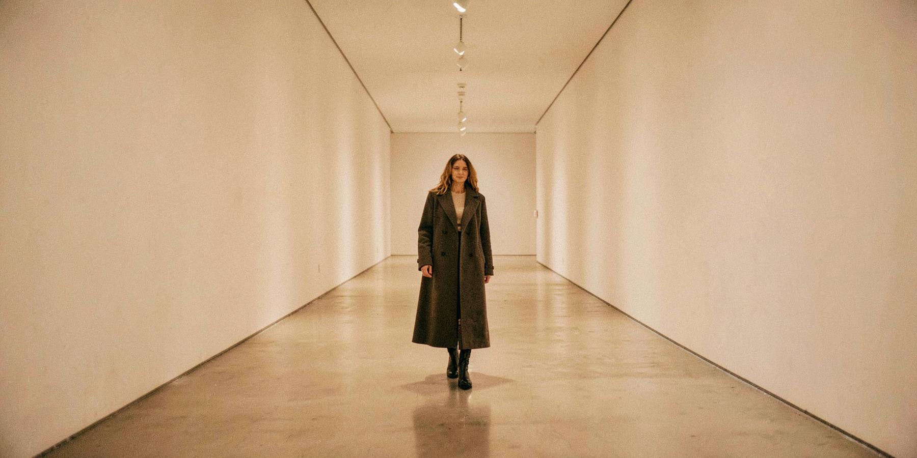Woman in a long coat in an empty gallery corridor